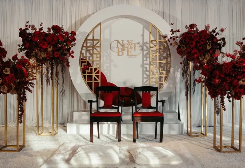 An indoor ceremony setting with red chairs, white curtains and floral arrangements